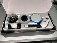 Box opened showing the electric cleaning spin brush handle and 8 different brush heads in molded plastic insert.