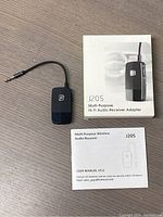 Black wireless Bluetooth audio receiver adapter with a short cable and 3.5mm audio jack, displayed alongside the J205 user manual.