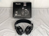 Front view of black Bluedio Turbine Bluetooth headphones with box behind them on white cloth background.