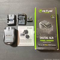 Charger unit, two interchangeable plug adapters, instruction manual, and original product box shown from above on dark background