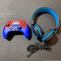 Wireless gaming controller and wired headphones together viewed from above on a black surface.