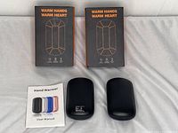 Two black Model A22 hand warmers with two user manuals and two packaging boxes. The boxes say 'Warm Hands Warm Heart' and show heating and rechargeable features.