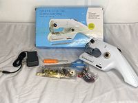 Handheld electric sewing machine with power adapter, screwdriver, scissors, extra bobbins, needles, thread spools, and box.