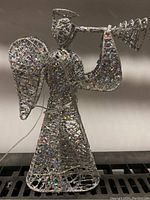 Front view of the wireframe Christmas angel holding a trumpet with holographic decoration and attached battery wire.