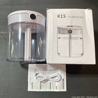 Photo showing the humidifier alongside its box, USB cable, and instruction manual laid out on a flat surface.