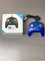 Front view of blue transparent Nintendo 64 controller next to its box with branding