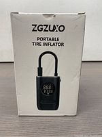 Front of the retail box showing the black portable tire inflator device with a digital display and U-shaped hose.