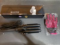 BLUETOP curling iron with three black ceramic barrels and ergonomic handle laid out with boxed packaging and heat protective glove in plastic.