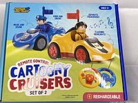 Box art showing two RC Cartoony Cruisers with cartoon police and bee drivers, highlighting features like horn, siren, flashing headlights, separate frequencies, and rechargeable battery.