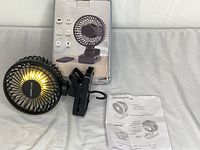 Small black portable clip fan displayed with original box and instruction manual, showing product condition and included materials.