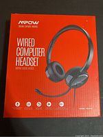 Front view of the MPOW wired computer headset box, showing product image and key features including noise-canceling mic, adjustable headband, compatibility, and model number PA071A.