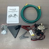Photo of the transfer pump with included accessories arranged on a flat surface: hose, funnel, clamps, battery clips, manual.