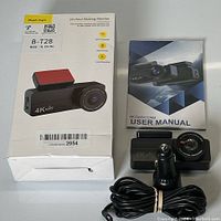 Contents of the lot including the dash cam unit with front lens and red mount pad, coiled car charger cable, and user manual.