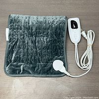 Electric heating pad shown from one side in dark gray plush fabric with attached controller and power cord.