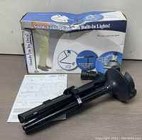 Black folded cane with triple leg design, built-in LED light, non-slip rubber tip, and original box with instruction manual on table.