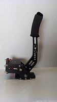 Front view of black metal gaming handbrake with ergonomic padded grip and detailed mechanical components.