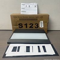 LED solar house number address light laid flat with a cardboard box labeled 'Solar House Number Address Light - LED' and white number templates in front.