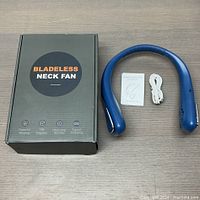 Box labeled 'Bladeless Neck Fan', blue neck fan device, white USB charging cable and instruction manual, all displayed on wooden surface.