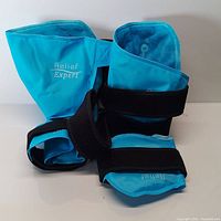 Photo showing two blue Relief Expert ankle foot ice pack wraps with black adjustable straps, displaying the front and inside lining.