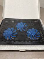 Black Havit laptop cooling pad with three visible blue fans inside black metal mesh, lying open in box with protective white wrap beneath.