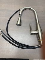 Full view of the faucet showing its curved design, pull-out spray head, and three braided water supply hoses.