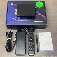 Fosi Audio Bluetooth Power Amplifier on its branded box, with remote control, power adapter, antenna, and user manual laid out for display.