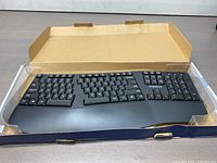 Insignia ergonomic wireless keyboard in original box, unpackaged showing split-key layout, cushioned wrist rest, and numeric keypad.