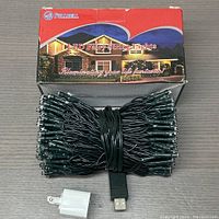 Coiled LED fairy string lights with USB plug adapter in front of box on wooden table.