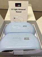 Photo showing two light blue Let’s Resin UV Light Advanced curing lamps in an open box with a printed manual behind them.