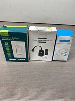 Three boxed items are shown on a wooden surface: Treatlife Ceiling Fan & Light Dimmer Switch, Outdoor Remote Control Outlet, and Outlet Extender with USB charger.