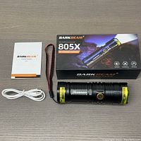 Darkbeam 805X flashlight with USB cable, wrist strap, and user manual laid out next to product box on a flat surface