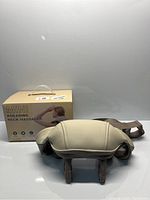 Front view of the beige and light brown mini neck massager device with its original packaging box in background.
