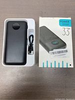 Black HX200J4 power bank and USB cable in white plastic tray next to the product box labeled POWER BANK 33+.