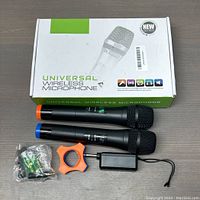 Set of two wireless microphones with colored rings and accessories displayed on table with box behind
