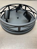 Side angled view of the black metal circular light fixture showing two spotlight sockets and the open decorative ring frame.