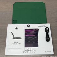 Green HOU MF-11 keyboard case, user manual, and black USB charging cable laid out on table.