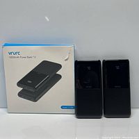 Box showing image and name of the Vrurc 10,000mAh Power Bank model T1168L and two power banks standing vertically side by side, with visible front LED display and brand name.
