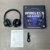 Photo showing headset next to instruction manual, USB charging cable, and product box with model and branding.