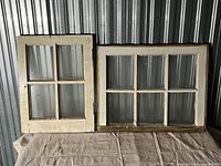 Two window frames side by side on a fabric-covered surface; one smaller 4-pane and one larger 6-pane frame, both with original glass panes.