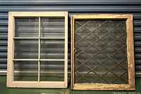 Front view of two window frames, one white with clear glass panes and one natural wood with diamond-pattern textured glass, leaned against a wall.