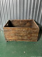 Side view of antique wooden kindling box showing aged wood surface and small wheels underneath