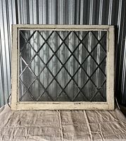 Front view of antique leaded glass window showing diamond pane pattern and wooden frame in worn cream paint.