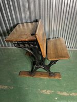 Side view of antique schoolhouse desk with wooden hinged desktop and bench, cast iron frame base.