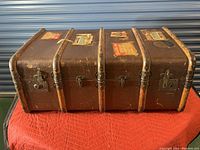 Closed view of the antique travel trunk showing exterior with wooden braces, metal locks, and vintage stickers on the surface.