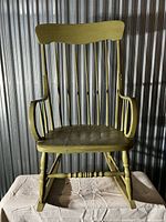 Front view of antique wooden rocking chair painted olive green showing spindle backrest and curved armrests.