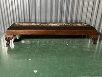 Side view showing the wooden base with carved legs and the embroidered floral needlepoint cushion top.