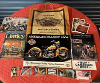 Assorted Harley-Davidson memorabilia arranged to show calendar, postcards, promotional pamphlets, paper bag, and motorcycle-themed images.