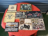 Full lot on red quilted blanket including 8 calendars and one framed print arranged in two rows, showing condition and variety of covers