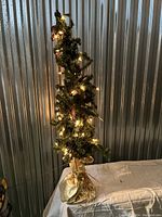 Full frontal view of mini tabletop Christmas tree with lights on, showing the densely packed pine needles and pine cones with gold fabric base.