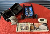 Overview of all items including the palm sander, luggage cart, box joint jig, and thermostat on a red quilted surface.